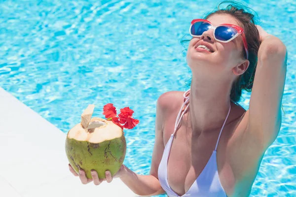 Bella giovane donna in occhiali da sole con cocktail di cocco in mano nella piscina di lusso — Foto Stock