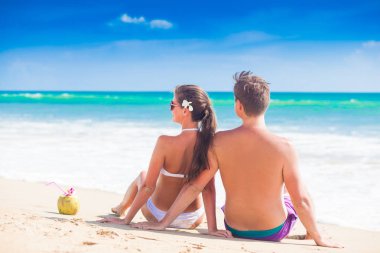 oturan ve tropikal bir plajda eğlenerek mutlu genç çift