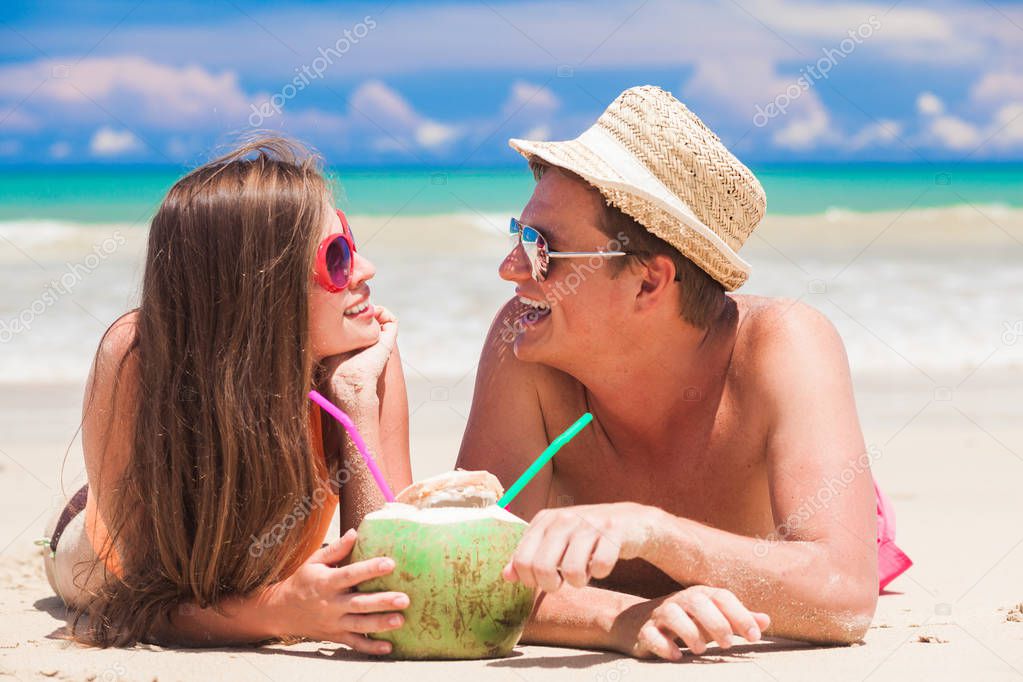 young couple relaxing at tropical beach with fresh coconut cocktails