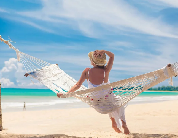 Ung kvinna i vit klänning avkopplande i en hängmatta vid stranden — Stockfoto