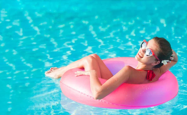 Mulher bonita que flutua com anel inflável de borracha rosa na piscina e se divertindo — Fotografia de Stock