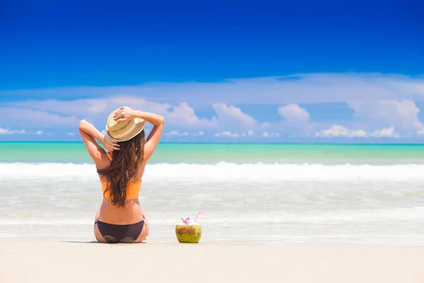 Lång haired kvinna i bikini och halm hat med färsk kokosnöt juice på tropical beach — Stockfoto