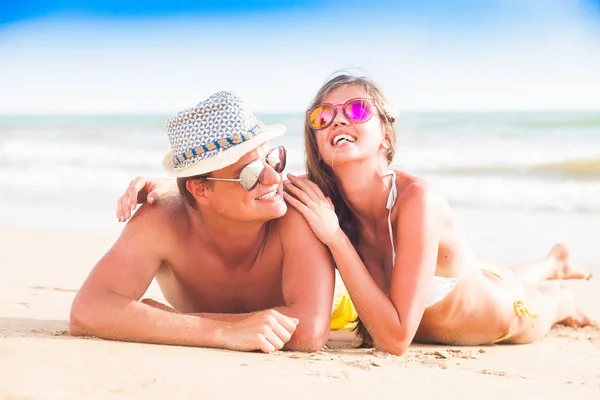 Portrait of happy young couple in straw hats lying and having fun on a tropical beach in the evening Royalty Free Stock Images