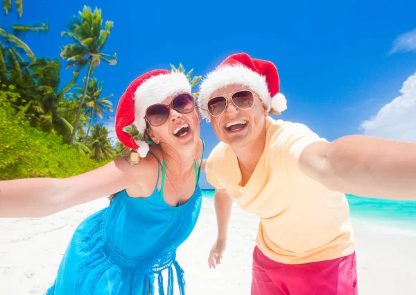 Νεαρό ζευγάρι στην καπέλα santa διασκεδάζοντας σε τροπική παραλία. νέο έτος, — Φωτογραφία Αρχείου