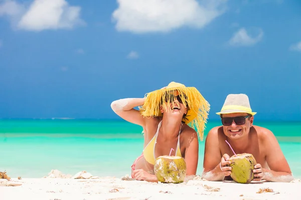 Счастливая молодая пара лежит на тропическом пляже в Барбадосе и пьет кокосовый коктейль — стоковое фото