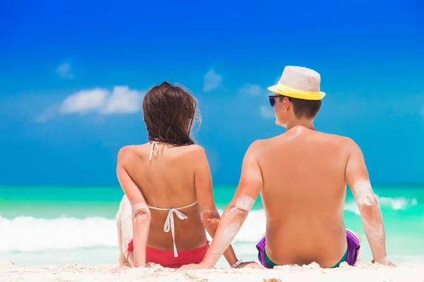 Vista posteriore di una coppia di uomini e donne seduti sulla spiaggia di sabbia bianca caraibica Foto Stock Royalty Free
