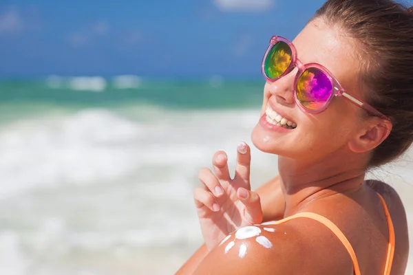 Nahaufnahme einer jungen Frau mit Sonnenbrille, die Sonnencreme auf die Schulter legt lizenzfreie Stockfotos