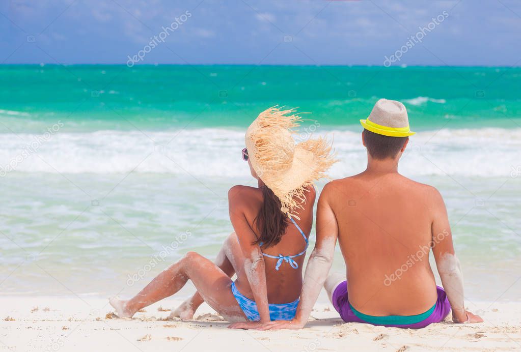 Back view of a man and woman couple sitting oncaribbean white sand beach