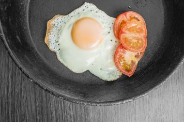 ahşap bir masa üzerinde bir dökme demir tavada doğranmış domates ile kızarmış yumurta kızarmış
