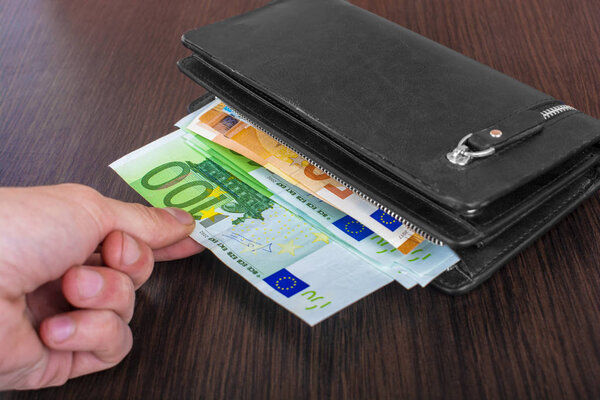 Рука человека вытаскивает купюры с кожаным кошельком и выводит европейскую валюту евро
 