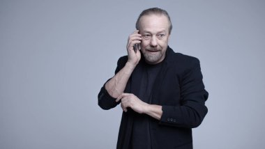 Neşeli, sakallı, beyaz adam telefonda konuşuyor.