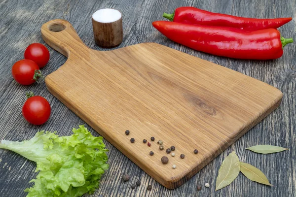 Oak cutting board with vegetables and spices on the kitchen table.