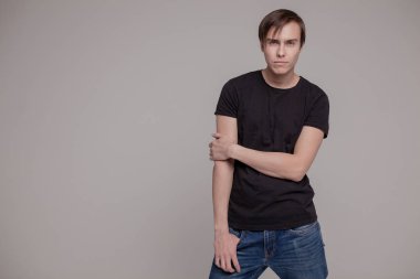 Gri arka planda duran genç adamın casual stüdyo portresi