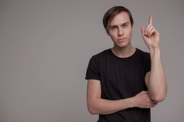 Gri arka planda duran genç adamın casual stüdyo portresi