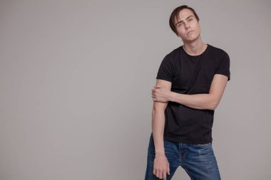 Gri arka planda duran genç adamın casual stüdyo portresi