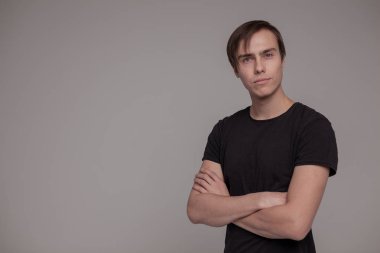 Gri arka planda duran genç adamın casual stüdyo portresi