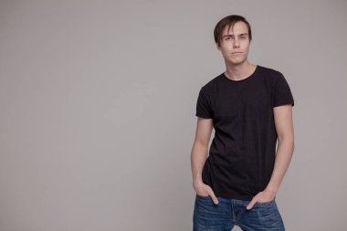 Gri arka planda duran genç adamın casual stüdyo portresi