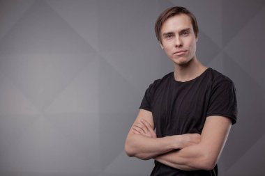 Gri arka planda duran genç adamın casual stüdyo portresi