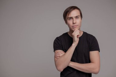 Gri arka planda duran genç adamın casual stüdyo portresi