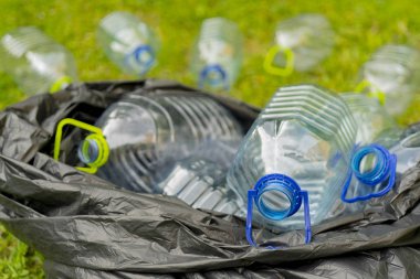Çöp torbasında çimenlerin üzerinde yatan boş plastik şişeler