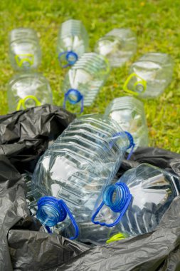 Çöp torbasında çimenlerin üzerinde yatan boş plastik şişeler