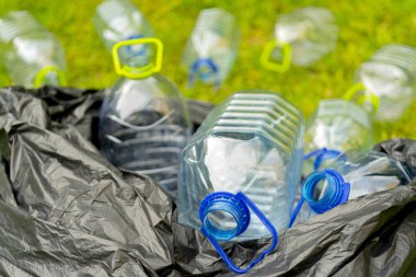 Çöp torbasında çimenlerin üzerinde yatan boş plastik şişeler