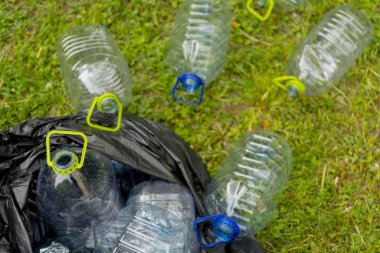 Çöp torbasında çimenlerin üzerinde yatan boş plastik şişeler