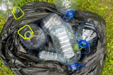 Çöp torbasında çimenlerin üzerinde yatan boş plastik şişeler