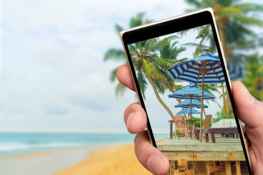 Akıllı telefon ekranında okyanus kenarındaki yazlık kafe. Tropiklerde güneşli bir gün.