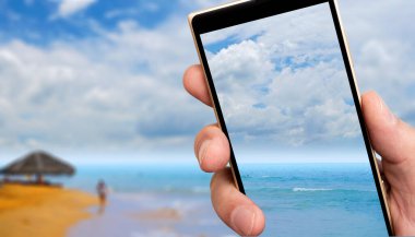 Akıllı telefon ekranında Sandy Ocean plajı. Tropiklerde güneşli bir gün.