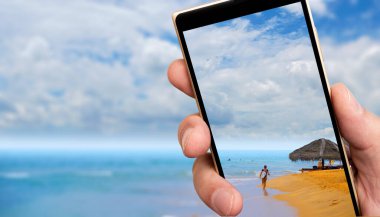 Akıllı telefon ekranında Sandy Ocean plajı. Tropiklerde güneşli bir gün.