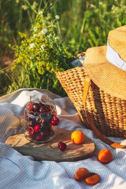 Güneş ışınları bir saman sepeti arka plan karşı şeffaf bir cam kavanozda iştah açıcı taze tatlı kiraz. Yaz meyveleri ve meyveleri - açık havada sağlıklı bir atıştırmalık. Yaz pikniği fikri