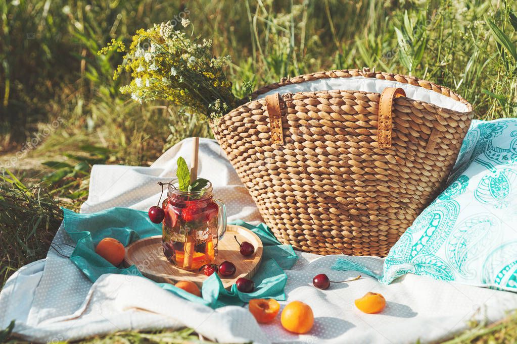 Lemonade in a glass goblet and with a bamboo straw, an eco-friendly summer picnic. Beautiful lemonade supply of fresh berries and fruits on the background of grass and a straw bag with flowers.