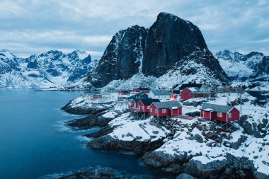 Karlı bir Norveç köyünde deniz ve dağlarla çevrili kırmızı kulübeler. Hamnoy.