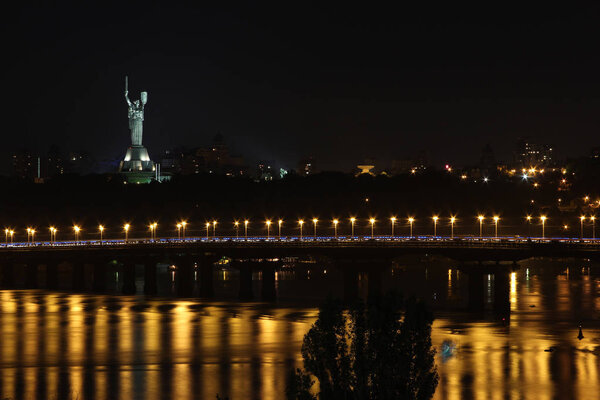 cityscape on the background of a bridge and a river with a beautifully lit statue