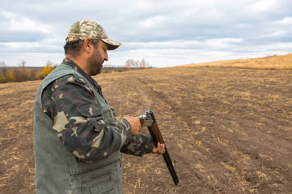 ハンターの帽子と 草原で獲物を捜して銃リロード武器 銃のバレルからの煙 — ストック写真