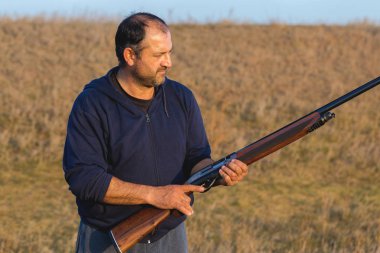 Adam silahlı kartuşları doğada vuruyor, avcı hedefe günbatımında vuruyor.