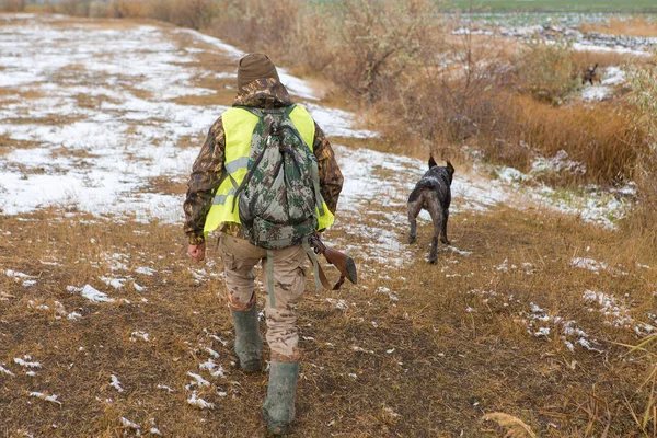 Şapkalı bir avcı kamuflaj silah ve bozkır köpek ile bir yansıtıcı yelek