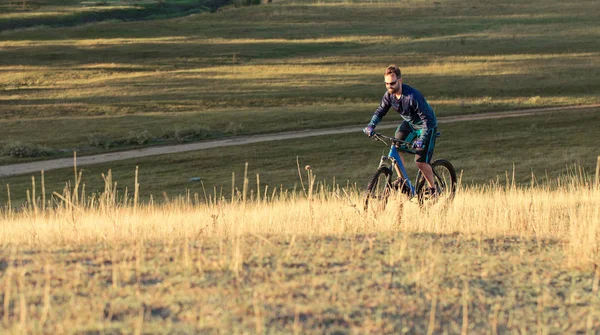 Cyclist in shorts and jersey on a modern carbon hardtail bike with an air suspension fork standing on a cliff against the background of fresh green spring forest