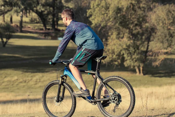 Cyclist in shorts and jersey on a modern carbon hardtail bike with an air suspension fork standing on a cliff against the background of fresh green spring forest