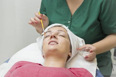 Yüz bakımı. Güzellik uzmanı güzellik salonunda fırça kullanarak yüzüne güzellik maskesi takıyor.