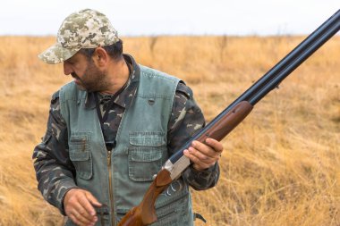 Şapkalı bir avcı kamuflaj silah ve bozkır köpek ile bir yansıtıcı yelek