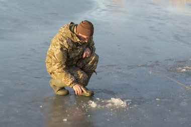 Kışın çukurda balık tutan adam küçük bir olta yakalar. Güzel bir kış gününde sazlıklarla gölde balık tutmak.