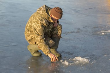 Kışın çukurda balık tutan adam küçük bir olta yakalar. Güzel bir kış gününde sazlıklarla gölde balık tutmak.
