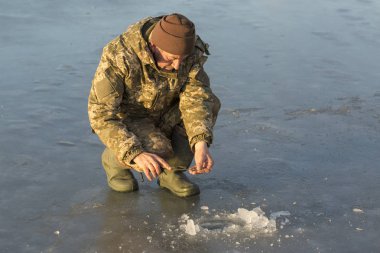 Kışın çukurda balık tutan adam küçük bir olta yakalar. Güzel bir kış gününde sazlıklarla gölde balık tutmak.