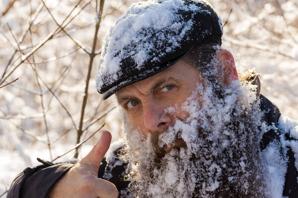 A man with a beard in the snow. Shows a thumbs up, delight.