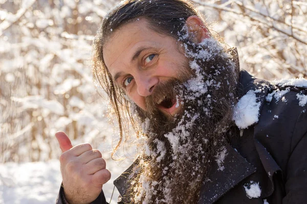 A man with a beard in the snow. Shows a thumbs up, delight.