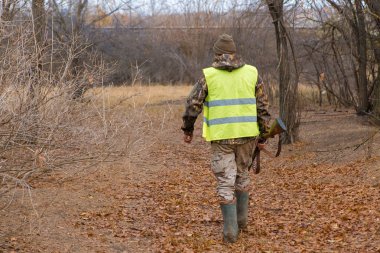 Silahlı bir avcı ve bir köpek bozkırda ilk kara çıkarlar yansıtıcı yelek giymiş sülün avlarlar.