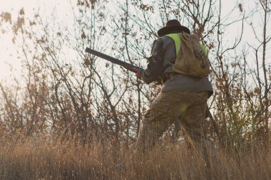 Şapkalı bir avcı kamuflaj silah ve bozkır bir yansıtıcı yelek