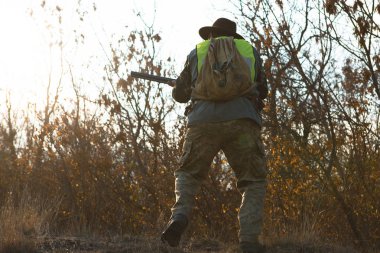 Elinde silah olan bir avcı silüeti. Şapkalı bir avcı kamuflaj silah ve bozkır bir yansıtıcı yelek
